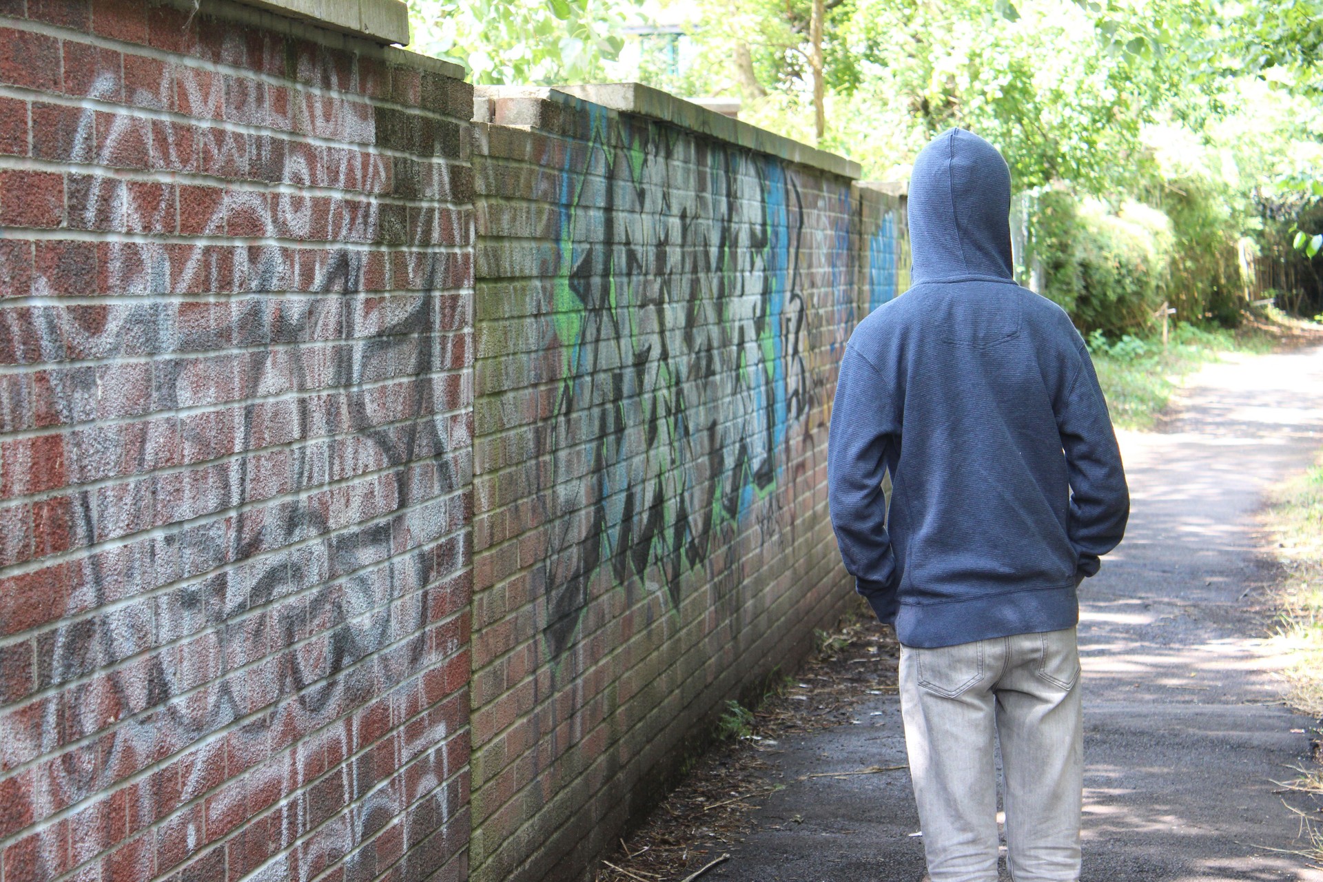 Image of teenage boy / youth wearing hoodie, beside graffiti wall